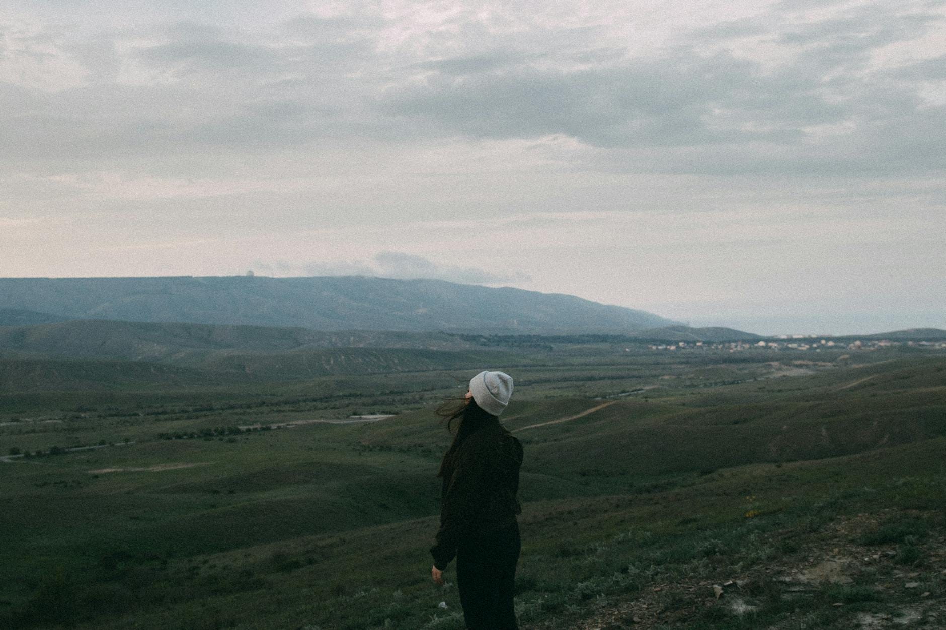 Kobieta na wzgórzu patrzy na górski krajobraz pod pochmurnym niebem