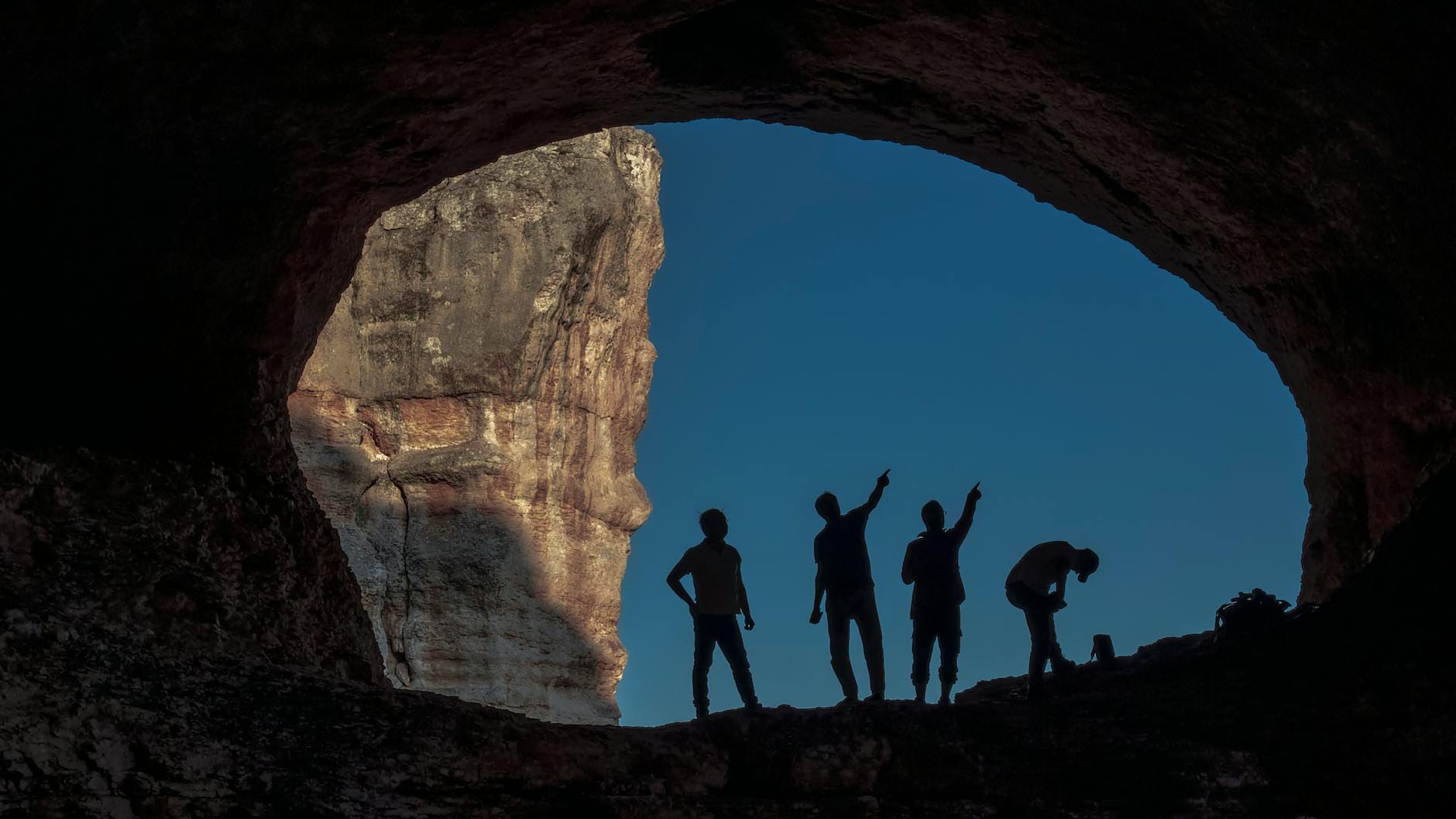 Sylwetki turystów w jaskini na tle błękitnego nieba