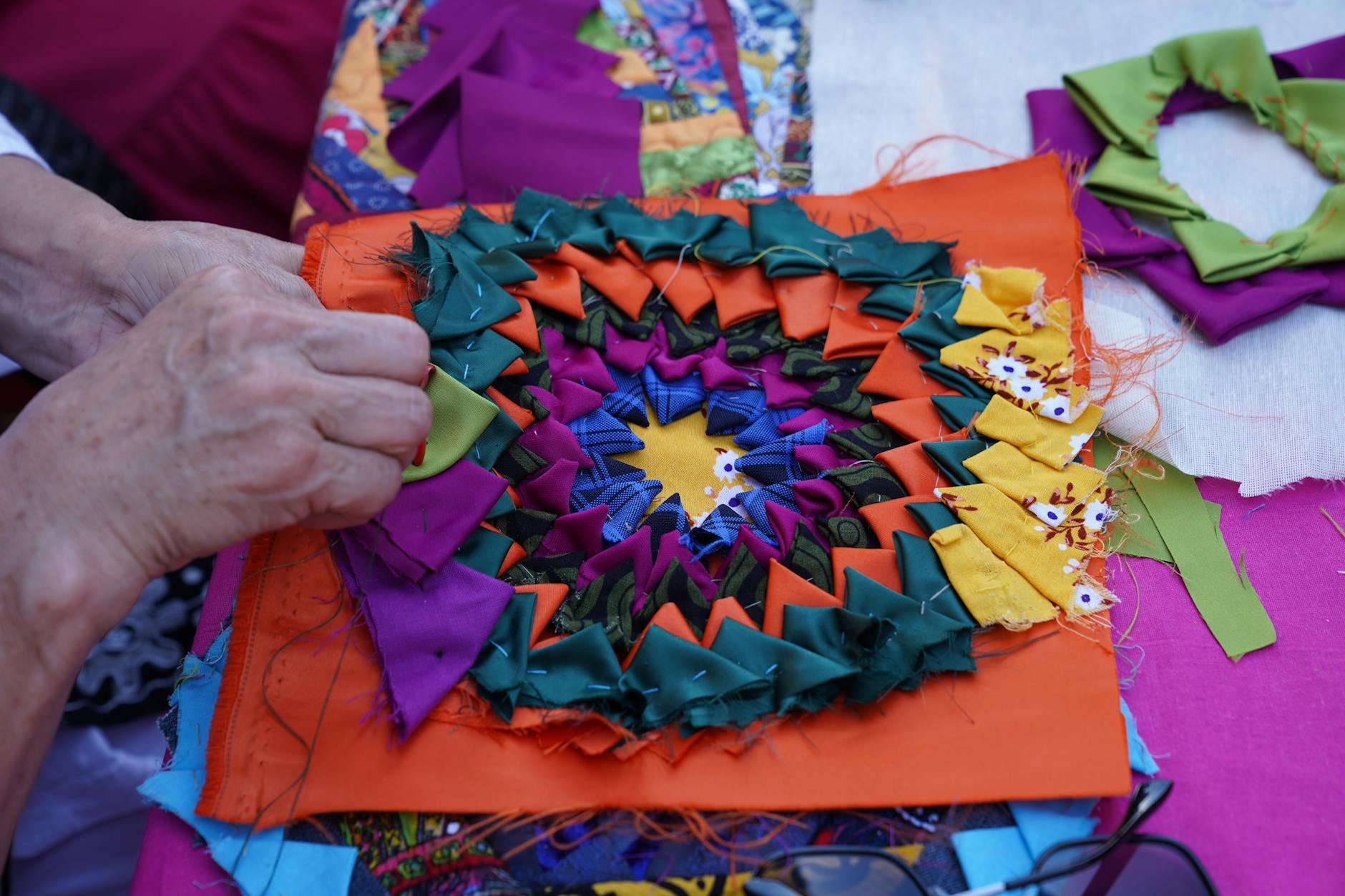 Dłonie układają kolorowe kawałki materiału w patchwork na stole